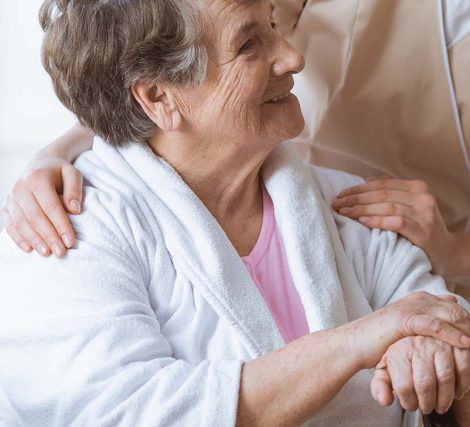 Elderly woman on wheelchair in nursing home with helpful doctor at her side and young nurse making the bed